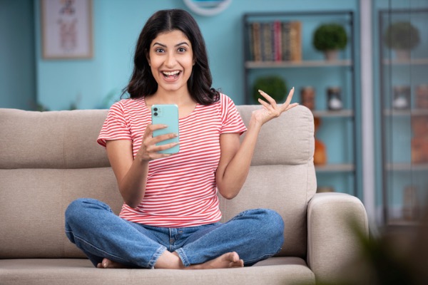 Excited woman sitting on couch with phone in hand.